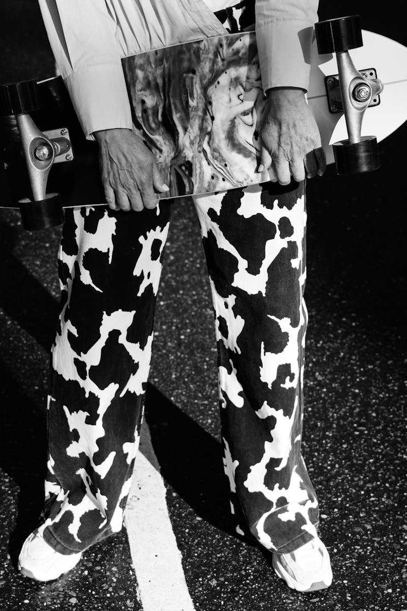 Black and white image of a person holding a skateboard with patterned pants.